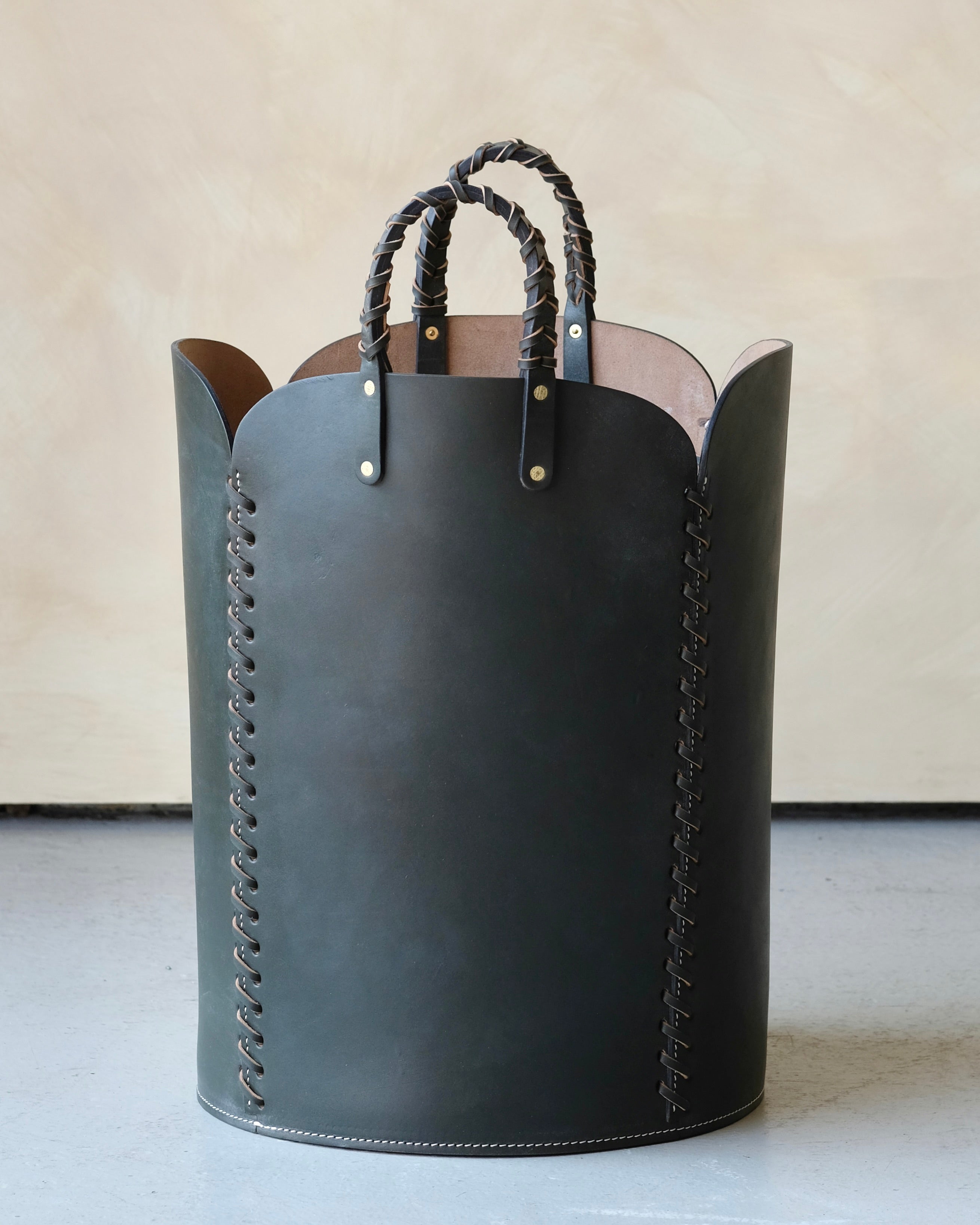 Dark green leather basket with braided handles on a light background