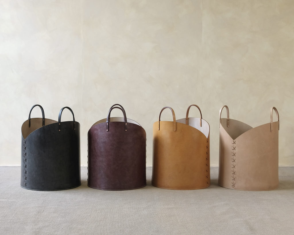 Four leather baskets in black, brown, tan, and beige on a neutral background