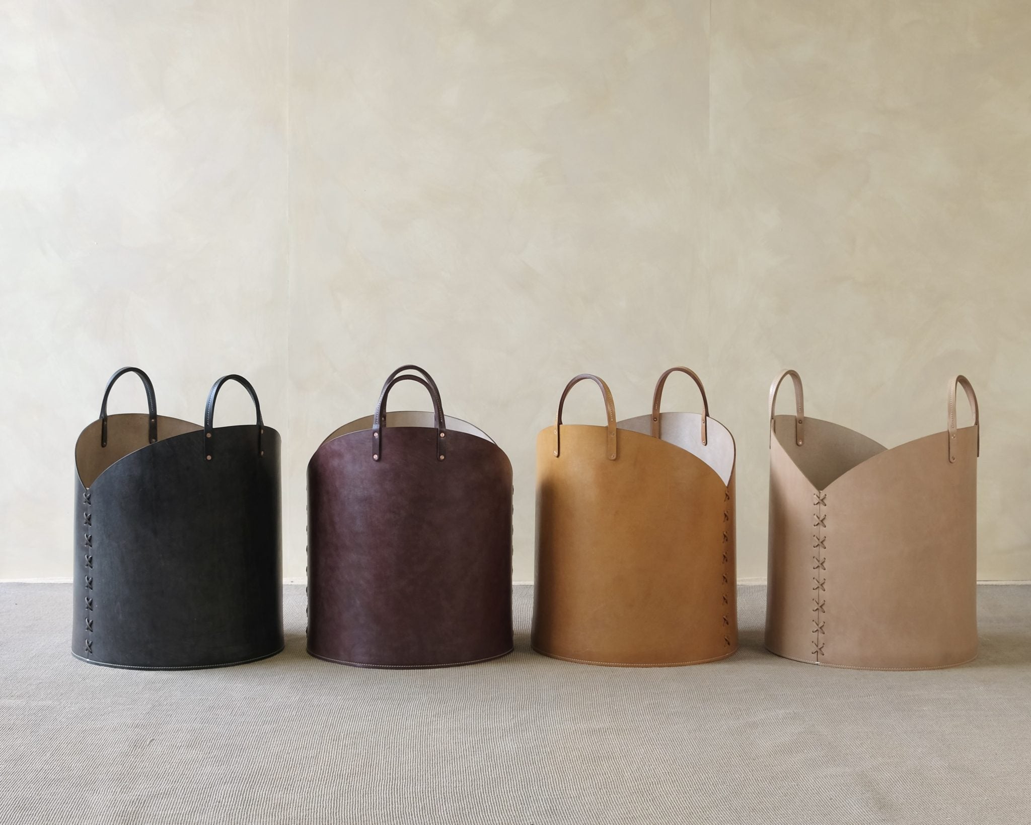 Four leather baskets in black, brown, tan, and beige on a neutral background