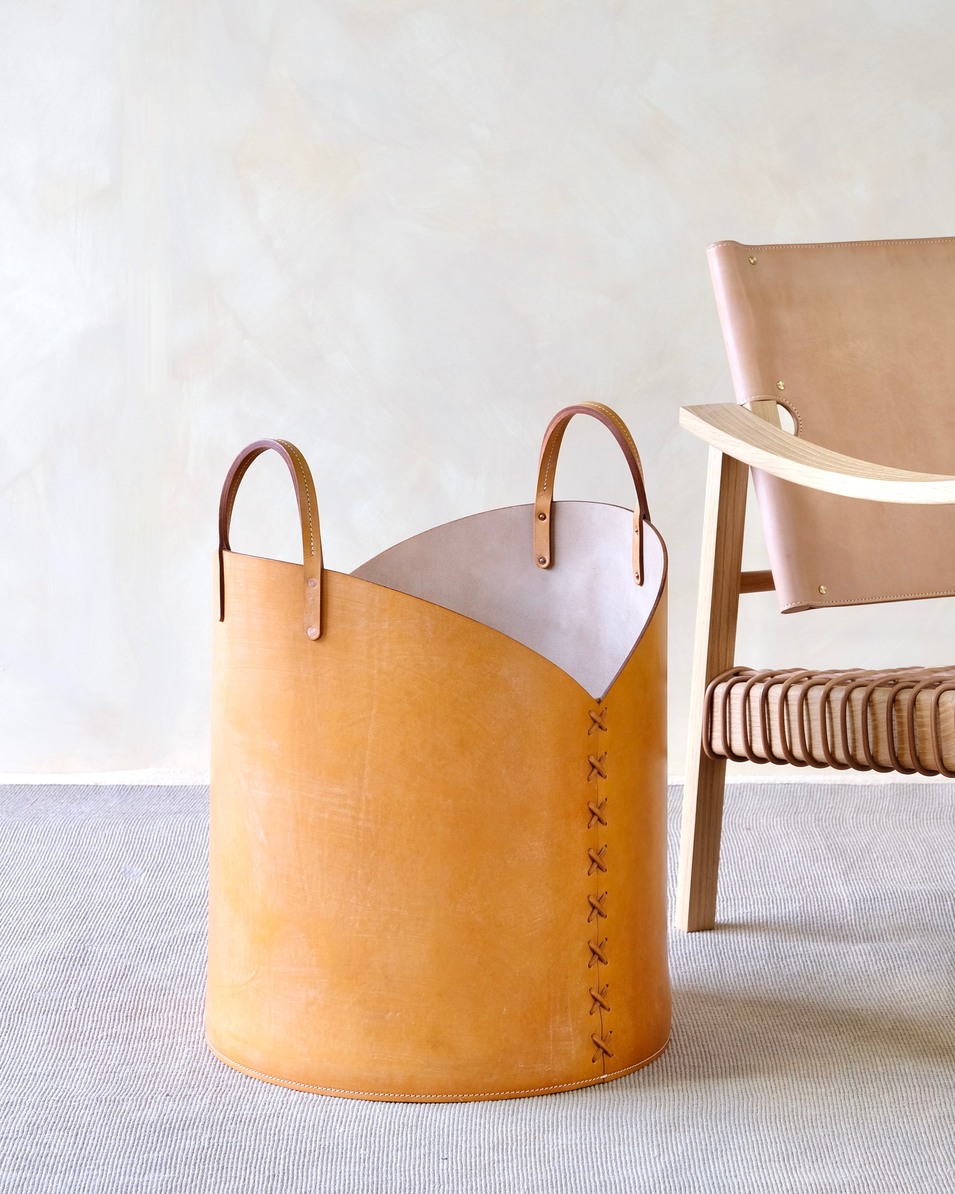 Tan leather basket with white top on a light surface, next to a wooden chair.