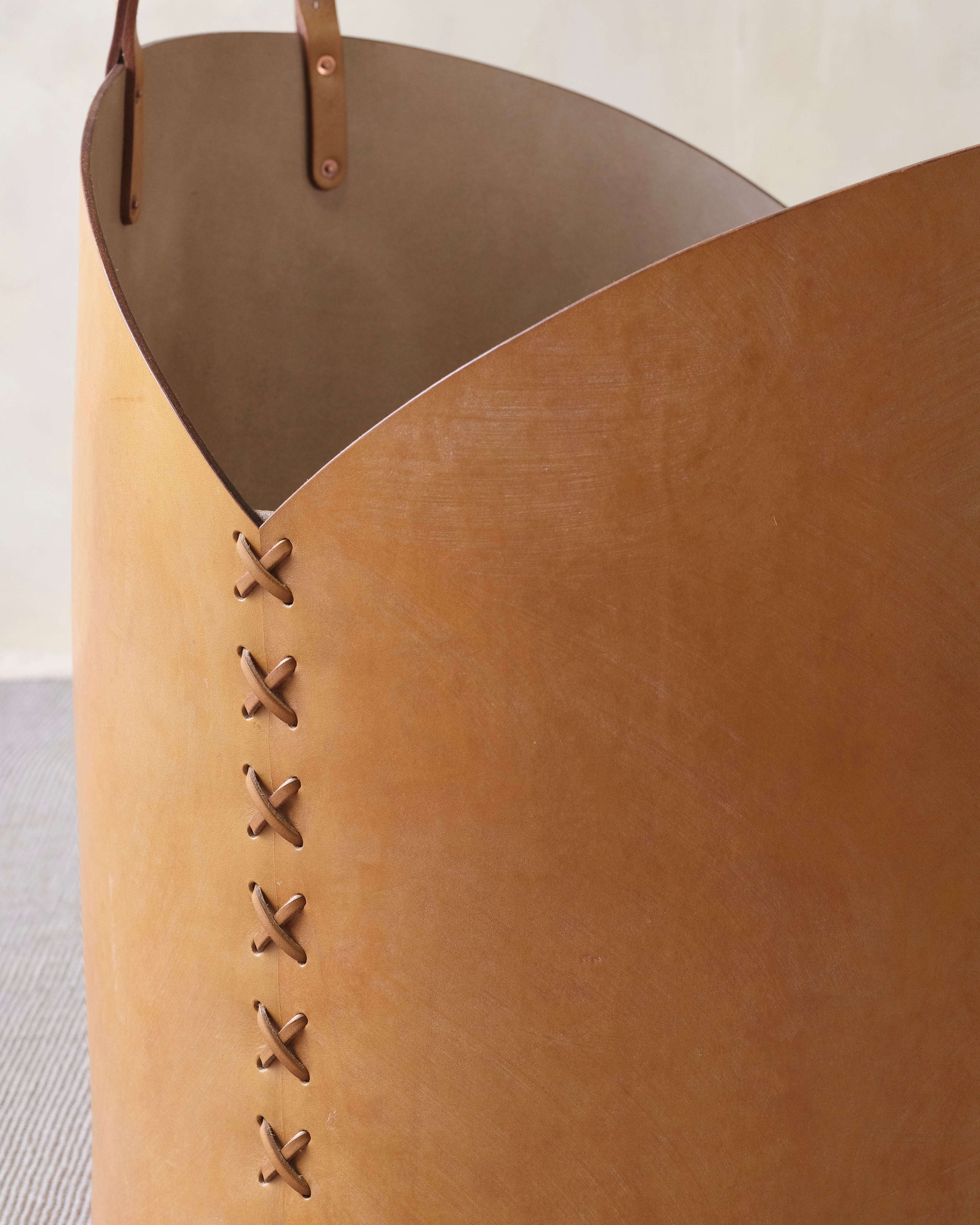 Close-up of a tan leather basket with brown accents and visible stitching on a light background.