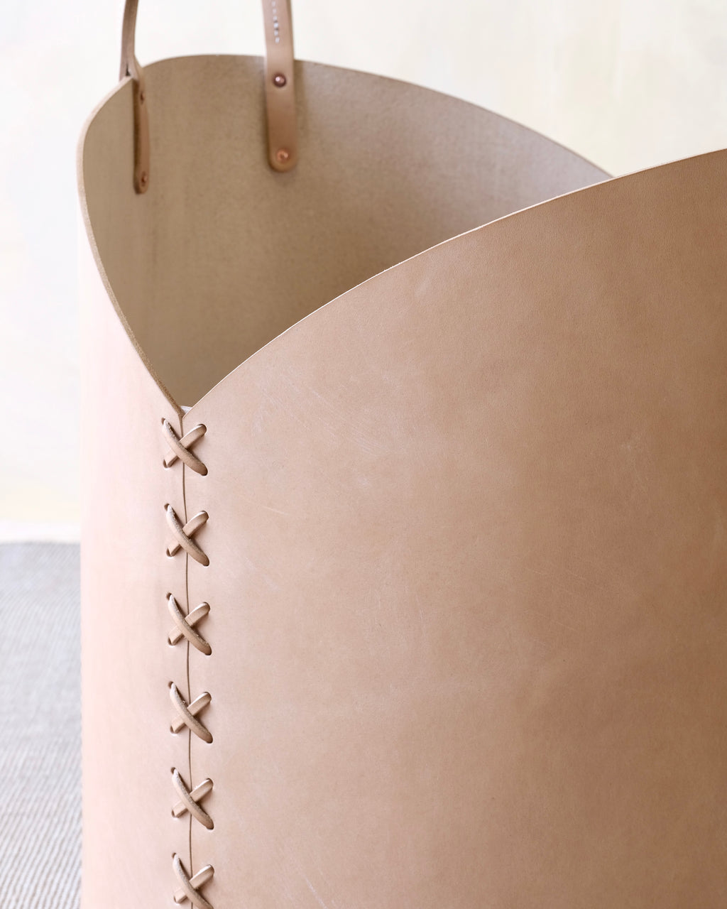 Close-up of a beige leather basket with brown handles and stitching details.