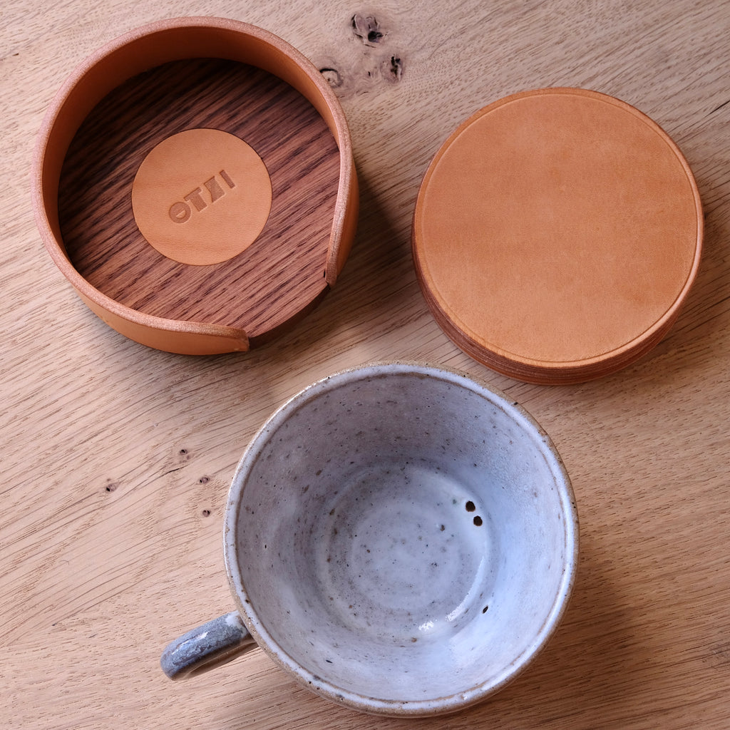 Ceramic mug with wooden coaster and leather coasters on a wooden surface