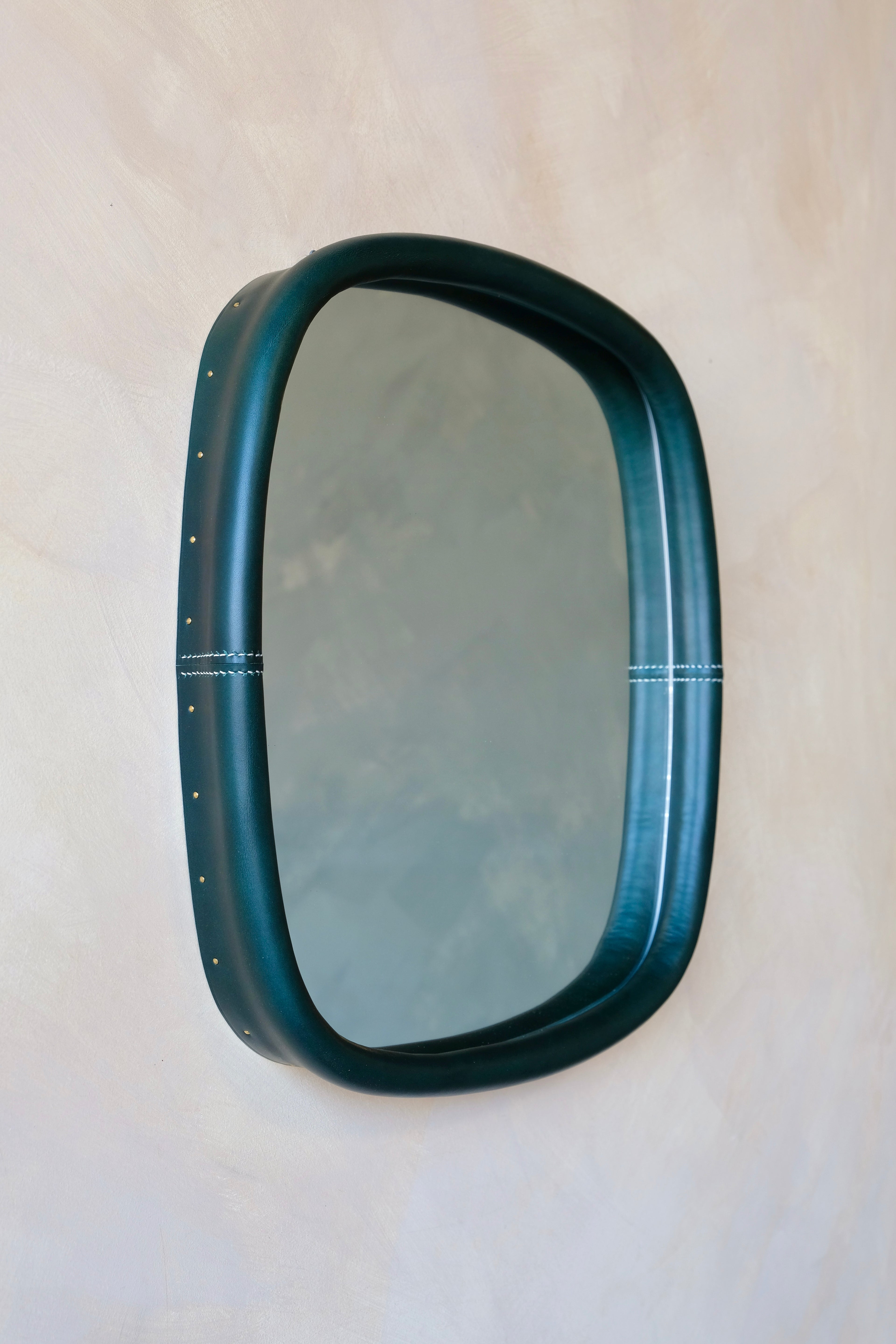 small square mirror with a dark green frame on a beige background