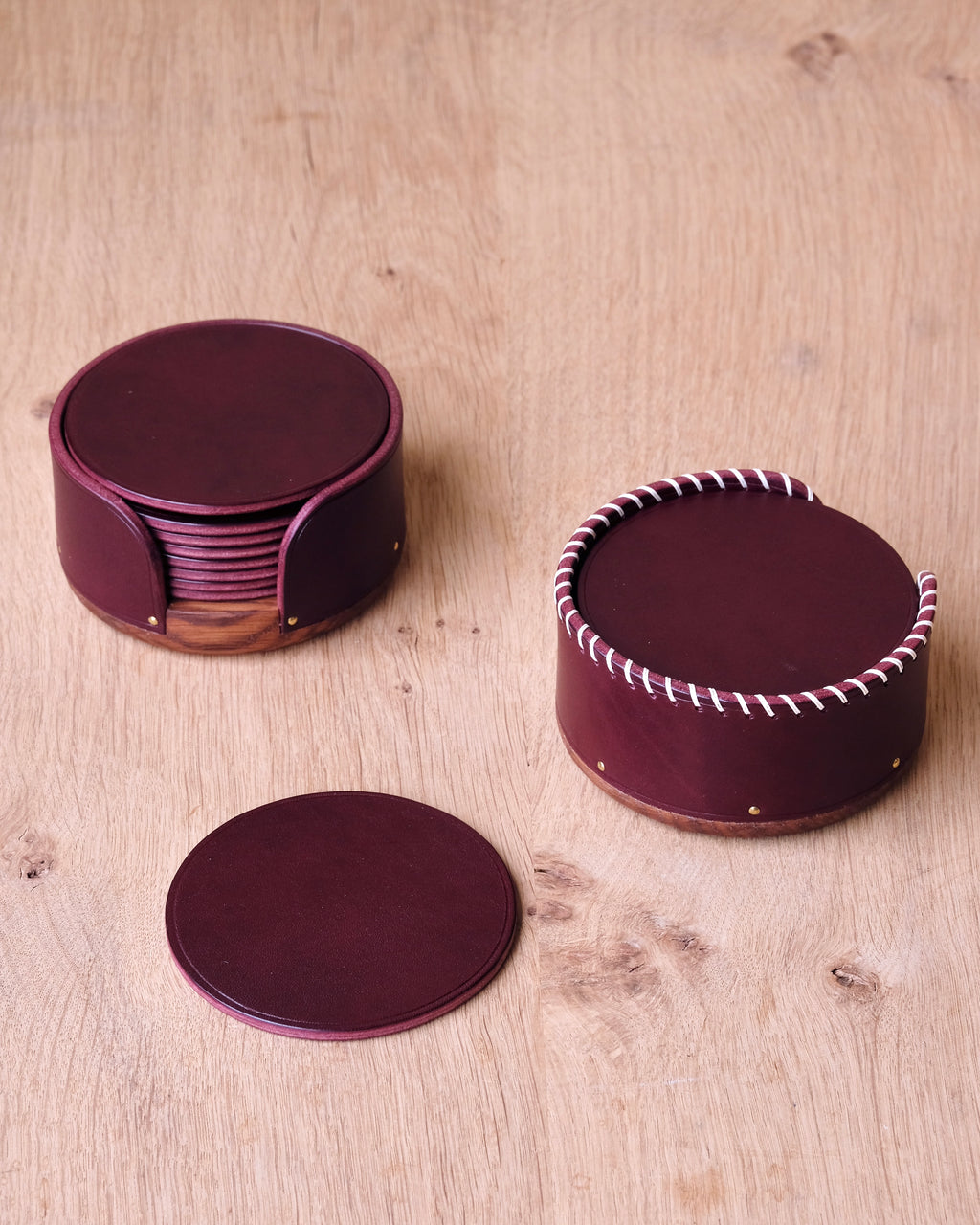 Set of burgundy leather coasters with a round container on a wooden surface
