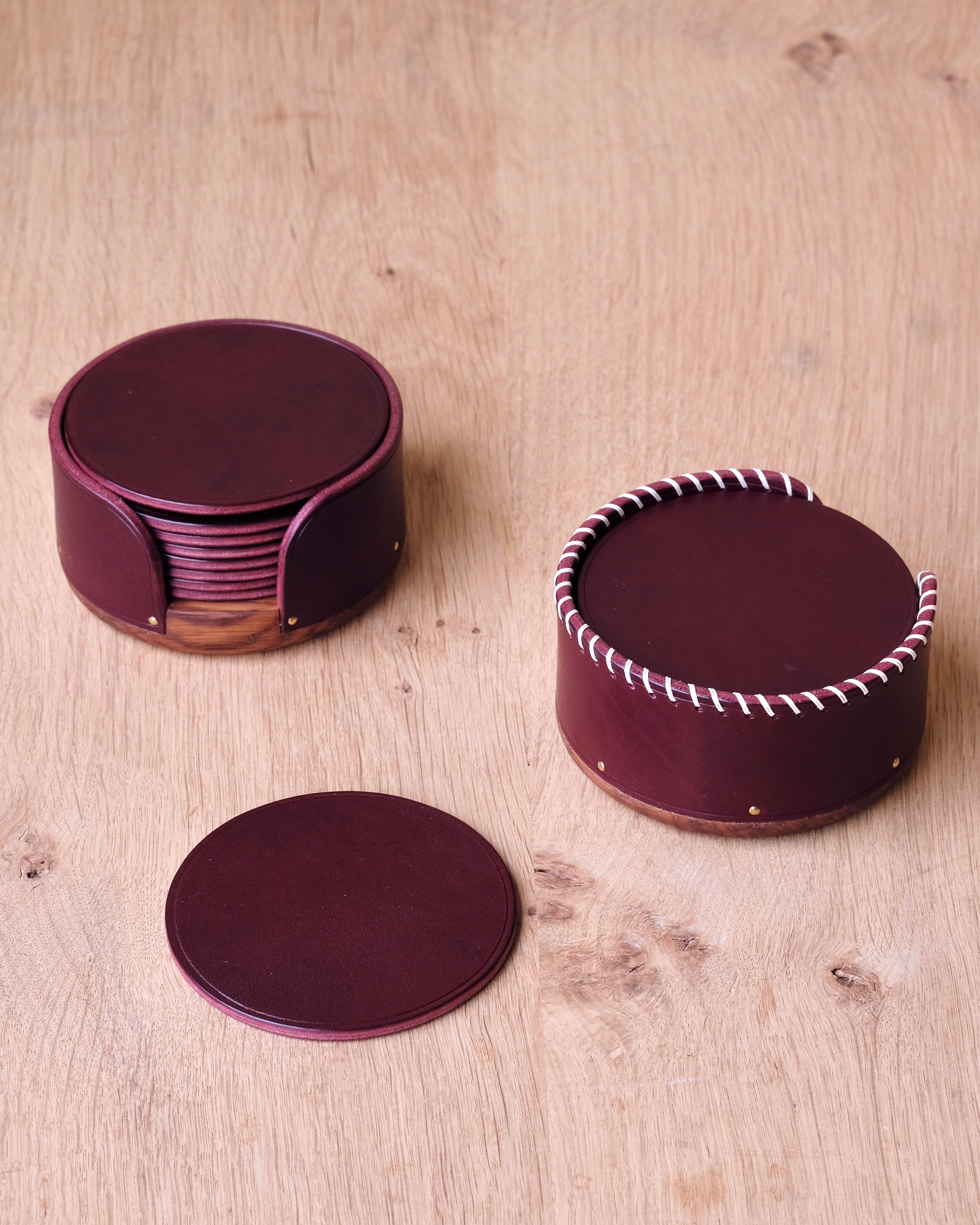 Set of burgundy leather coasters with a round container on a wooden surface